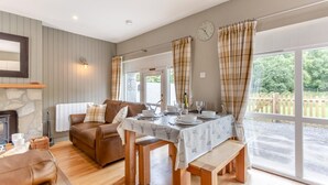 Una sala de estar acogedora con chimenea, una mesa de comedor preparada para cuatro personas y un ventanal con cortinas.