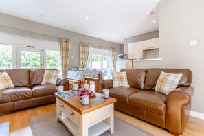 A cozy living room with two brown leather sofas, a wooden coffee table, and a dining area with a table set for two. - 2 Bed in Newtonmore (oc-e32418) (Newtonmore)
