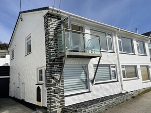 A two-story house with a stone facade, a balcony with glass railings, and a garage door. - 2 Bed in Porthleven (oc-p00866) (Porthleven)