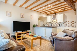 A living room with a television, leather sofa, wooden coffee table, and a kitchen in the background.
