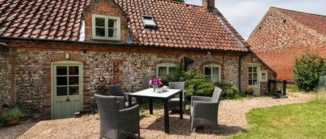 A stone house with a tiled roof, a gravel patio, and wicker furniture.