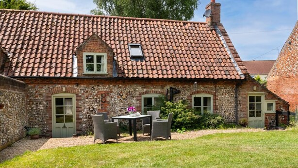 A stone house with a tiled roof, a small garden with a table and chairs, and a green door. - 2 Bed in North Creake (oc-2127) (North Creake)