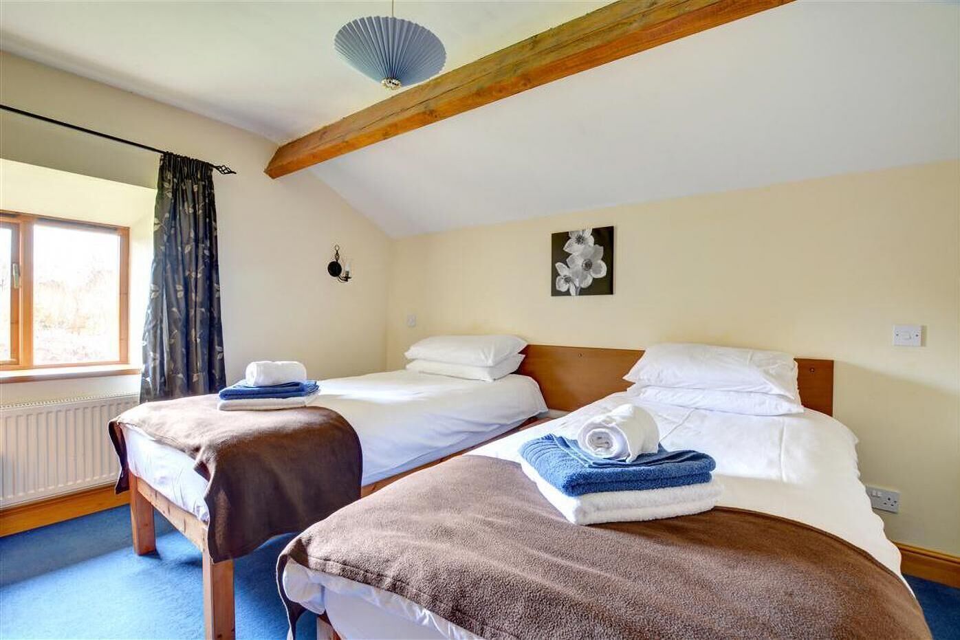 Ein Hotelzimmer mit zwei Betten, einem Fenster mit Vorhängen, einem Heizkörper und einem Deckenventilator.