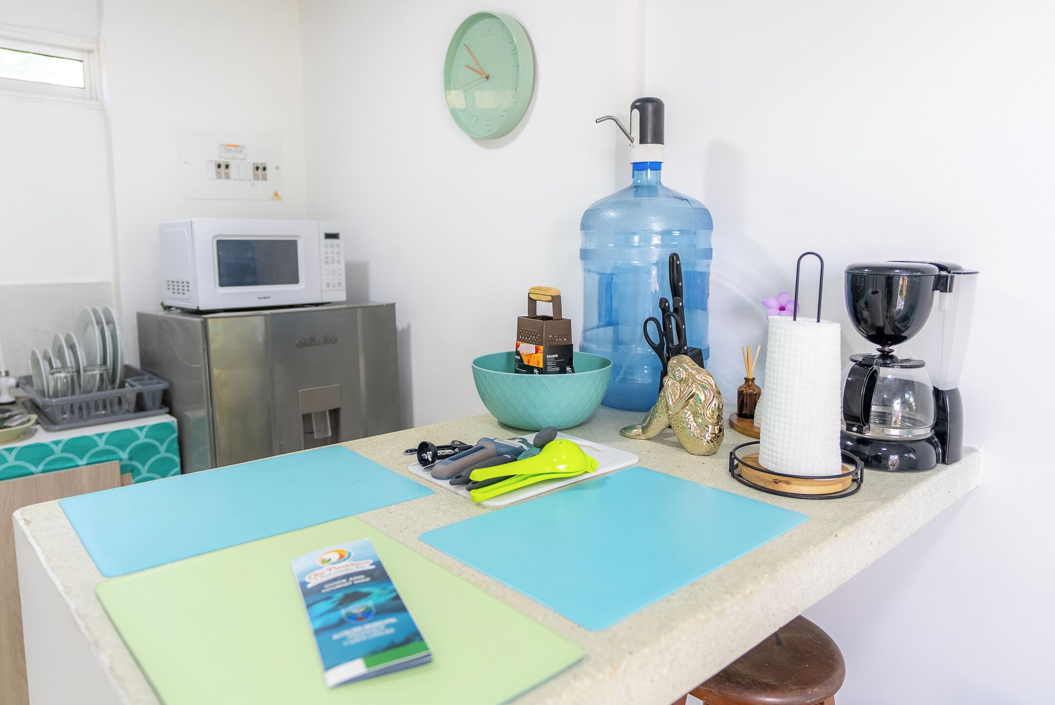 A kitchen counter with a microwave, large water dispenser, coffee maker, and various kitchen utensils.