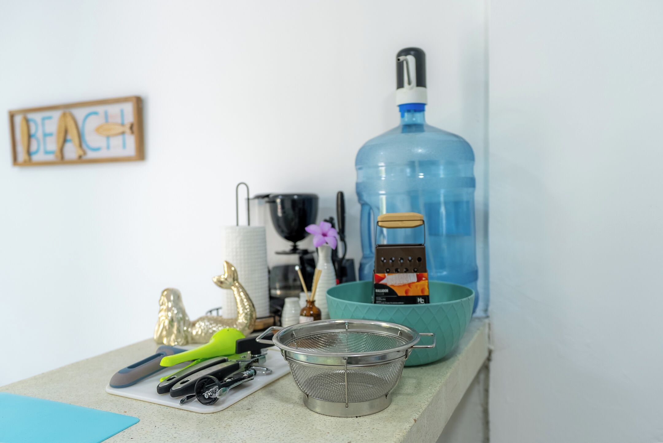 A kitchen counter with a large blue water bottle, a metal strainer, and various kitchen utensils.