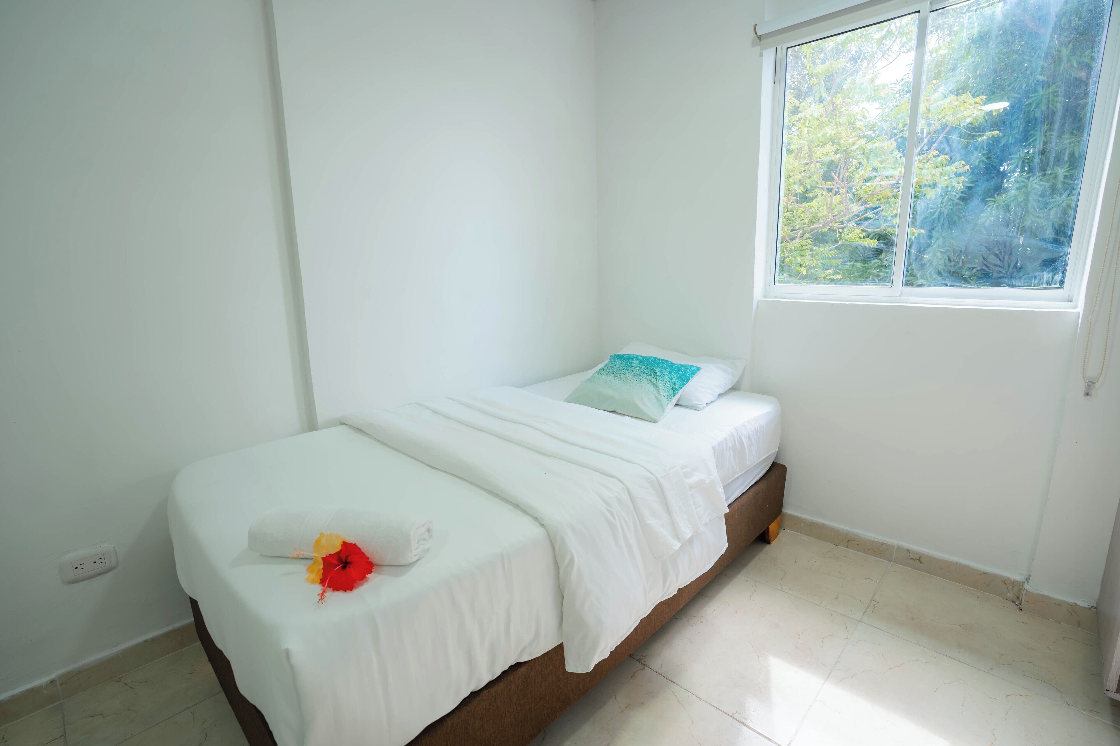 A single bed with white bedding, a pillow, and a decorative flower.
