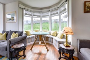 A corner room with a bay window, a round table, two sofas, and a lamp. - 5 Bed in Beadnell (oc-gd1901) (Beadnell)