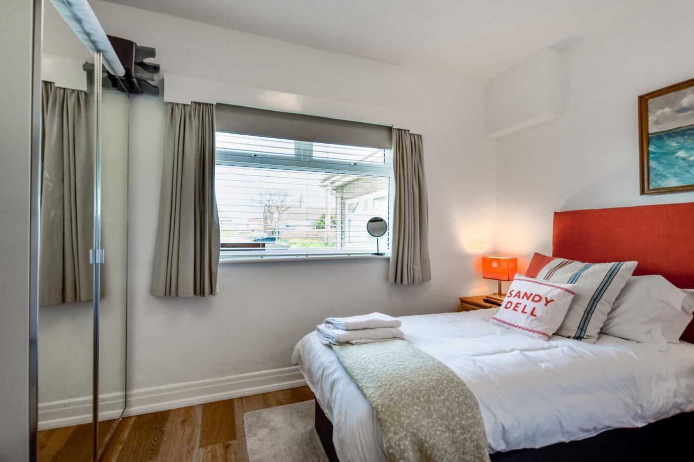 A bedroom with a bed, a window with curtains, a bedside lamp, and a painting on the wall.