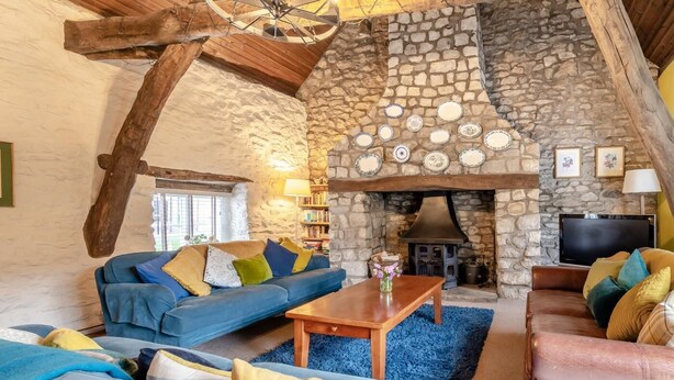 Ein gemütliches Wohnzimmer mit Kamin aus Stein, blauen Sofas und einem Fernseher.