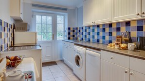 Une cuisine avec des meubles blancs, un lave-linge, un évier et une fenêtre.