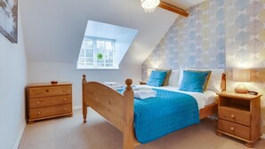 Une chambre avec un plafond en pente, un puits de lumière, un lit avec une literie bleue, des meubles en bois et un mur à motifs.