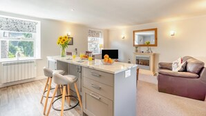 A modern kitchen with a central island, bar stools, a dining area with a sofa, and a fireplace.