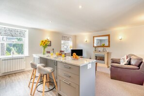 A modern kitchen with a central island, bar stools, a dining area with a sofa, and a fireplace.