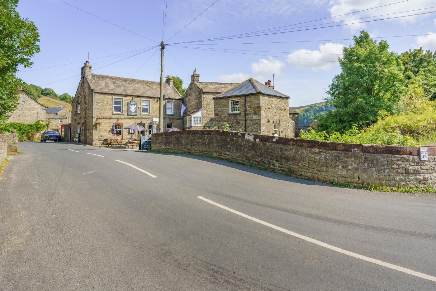 A stone building with a signboard, a paved road, and a stone wall.