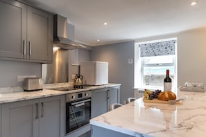 A modern kitchen with grey cabinets, a built-in oven, a stainless steel range hood, and a marble countertop.