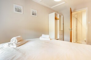 Hotellihuone, jossa on sänky, kaksi kehystettyä kuvaa seinällä, vaatekaappi ja suihkutila.