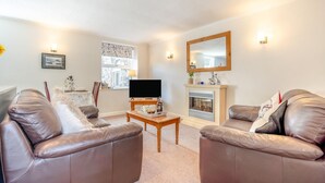 A living room with leather sofas, a flat-screen TV, a fireplace, and wall-mounted lights.