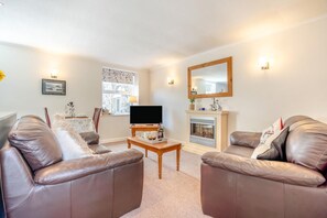 A living room with leather sofas, a flat-screen TV, a fireplace, and wall-mounted lights.