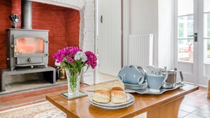 A cozy room with a fireplace, a table with pastries and a vase of flowers, and a set of blue teapots. - 2 Bed in Yatton (oc-s32603) (Leinthall Earls)