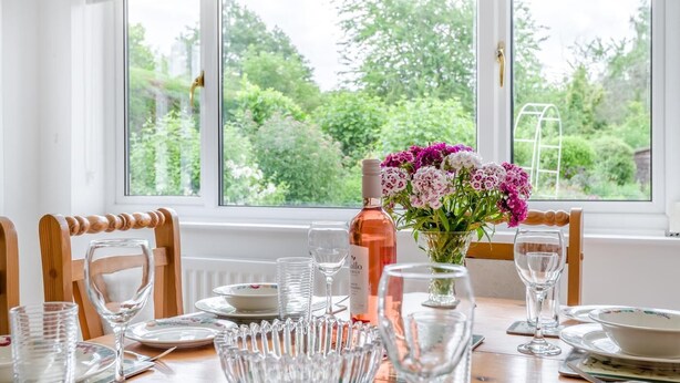A dining table set for six with a vase of flowers, a bottle of wine, and clear glassware. - 2 Bed in Yatton (oc-s32603) (Leinthall Earls)