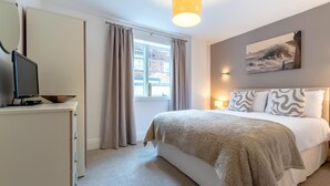 A bedroom with a bed, a television on a cabinet, a window with curtains, and a painting on the wall. - 2 Bed in Whitby (oc-w814) (Whitby)