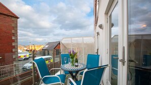 A balcony with a table and chairs, a bottle of champagne, and a vase of flowers. - 2 Bed in Whitby (oc-w814) (Whitby)