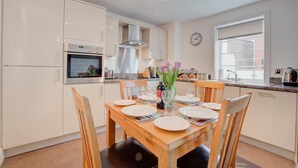A modern kitchen with white cabinets, a built-in oven, and a dining area with a wooden table set for two. - 2 Bed in Whitby (oc-w814) (Whitby)