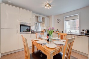 A modern kitchen with white cabinets, a built-in oven, and a dining area with a wooden table set for two. - 2 Bed in Whitby (oc-w814) (Whitby)