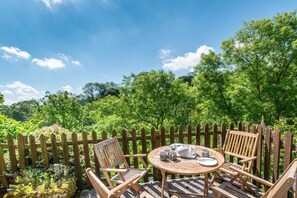 A wooden deck with a round table and chairs, surrounded by a wooden fence, overlooking a lush green forest. - 3 Bed in Bakewell (oc-dckno) (Youlgreave)