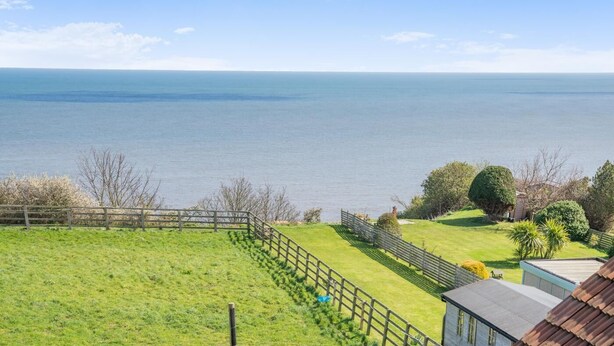 A coastal view with a grassy area, a wooden fence, and a building with a sloped roof. - 3 Bed in Whitby (oc-r565) (Robin Hood's Bay)