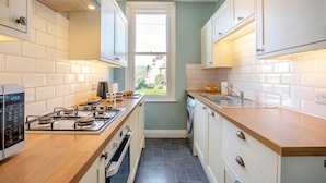 A compact kitchen with a gas stove, oven, and a window providing a view of the outside. - 3 Bed in Whitby (oc-r565) (Robin Hood's Bay)