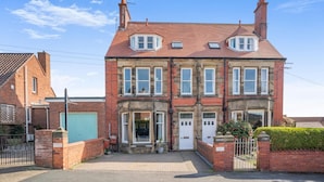 A two-story red brick house with a bay window, a front door, and a small garden area. - 3 Bed in Whitby (oc-r565) (Robin Hood's Bay)