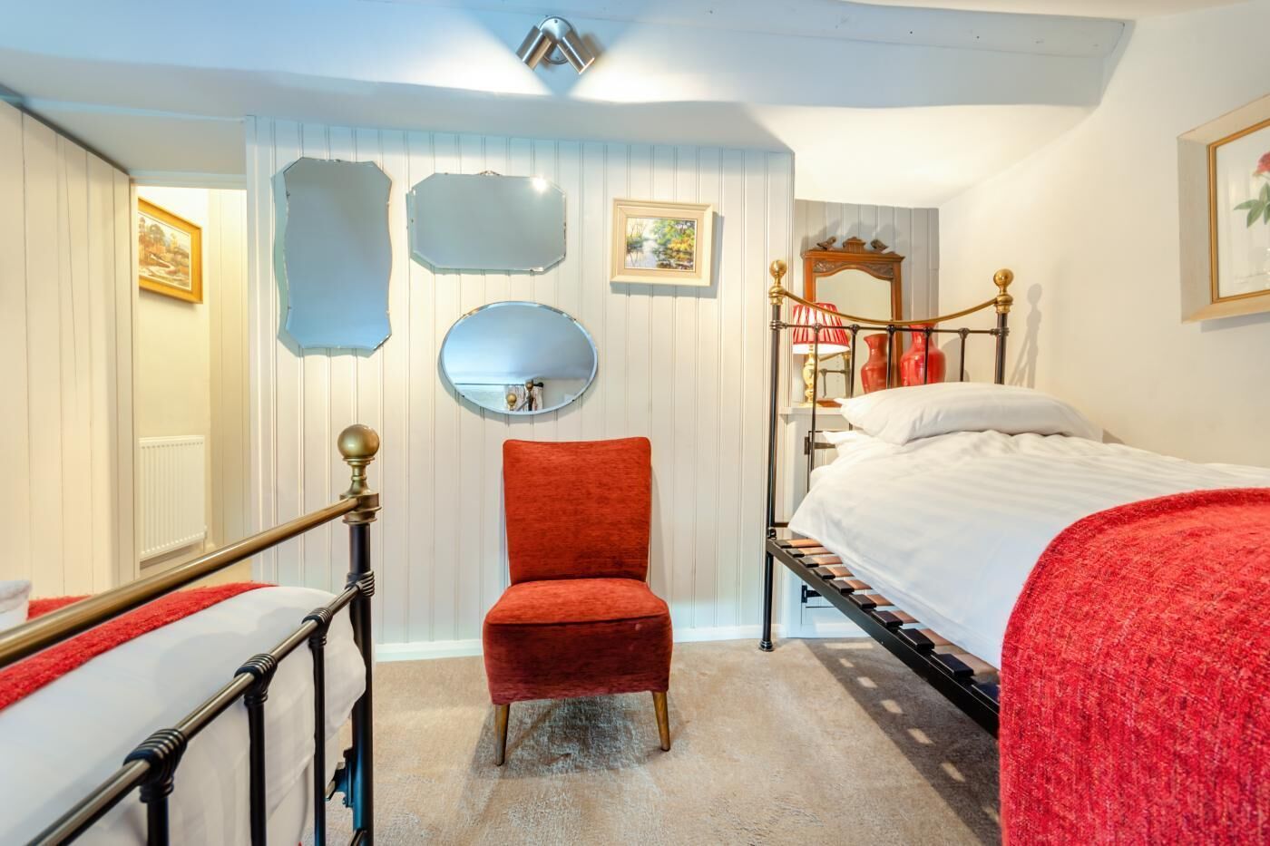 A bedroom with a bed, a red chair, a mirror, and a radiator.