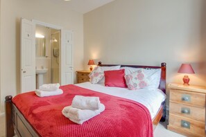 Ein Schlafzimmer mit einem Bett, zwei Nachttischen, einem Schrank und einem Badezimmer mit Waschbecken und Spiegel.