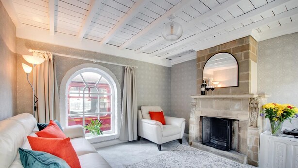 A living room with a fireplace, a sofa, a chair, and a large window. - 2 Bed in Whitby (oc-wa032) (Grosmont)