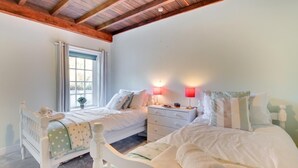 A bedroom with two beds, a window with curtains, a bedside table with lamps, and a wooden ceiling. - 2 Bed in Whitby (oc-wa032) (Grosmont)