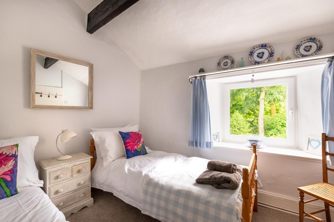 A bedroom with a bed, bedside tables, a mirror, a window with curtains, and a chair.