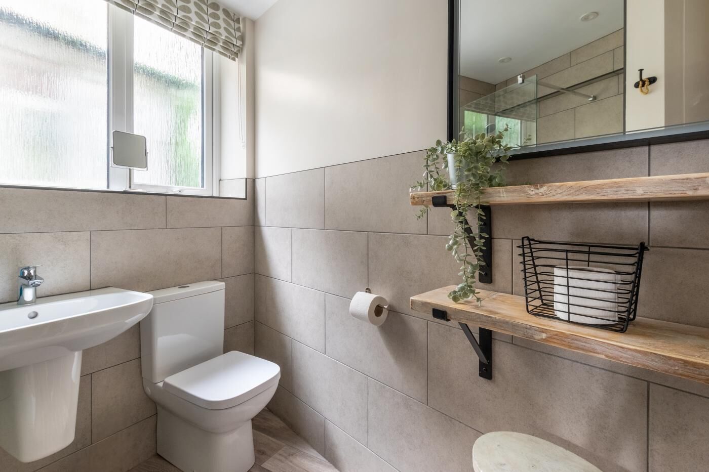 A bathroom with a toilet, sink, and shelves with a plant and a basket.