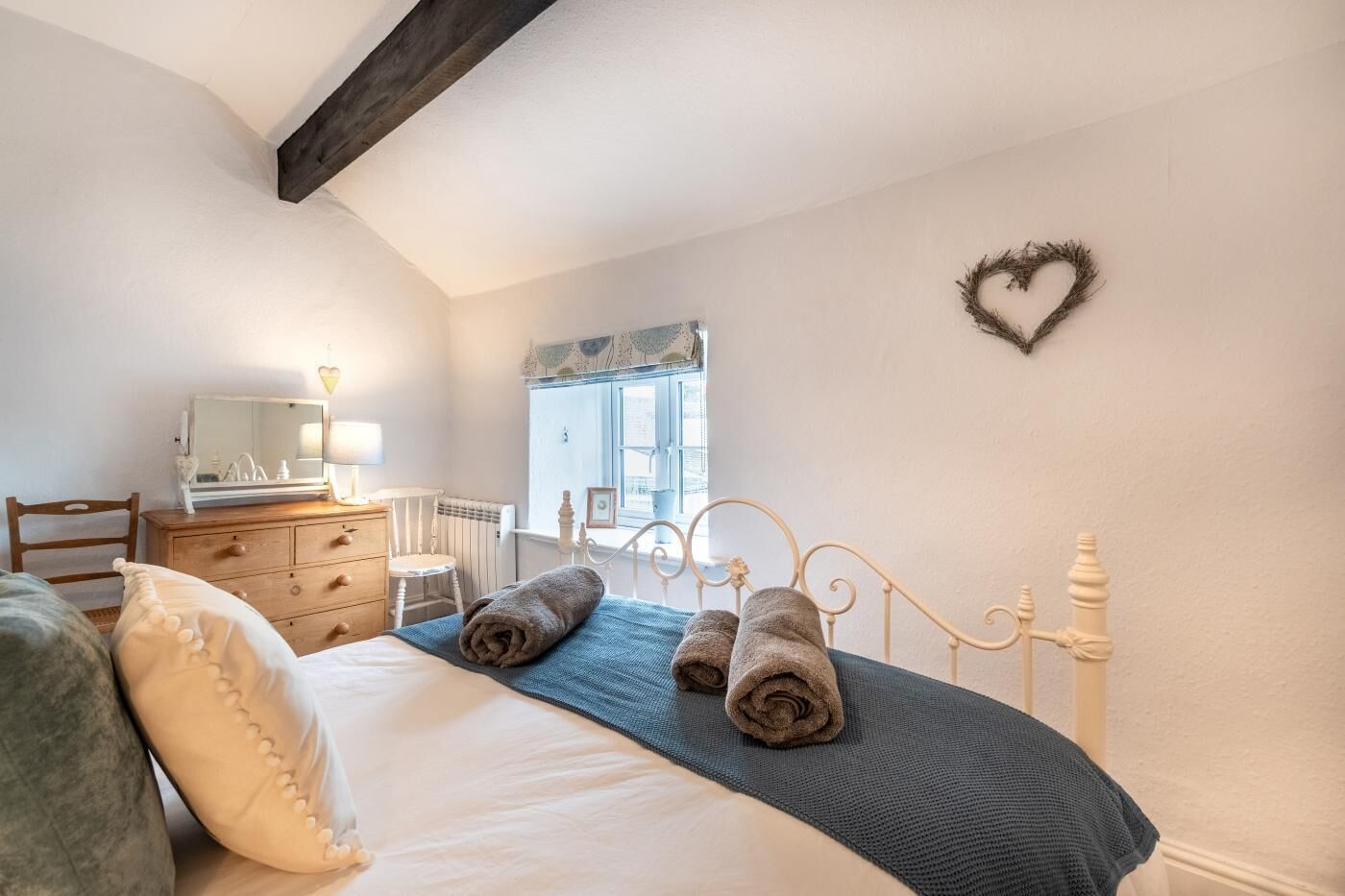 A bedroom with a bed, a dresser, a mirror, a window, and a heart-shaped decoration on the wall.