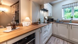 Una cocina moderna con encimera de madera, armarios blancos, horno empotrado y ventana con vistas a la vegetación.