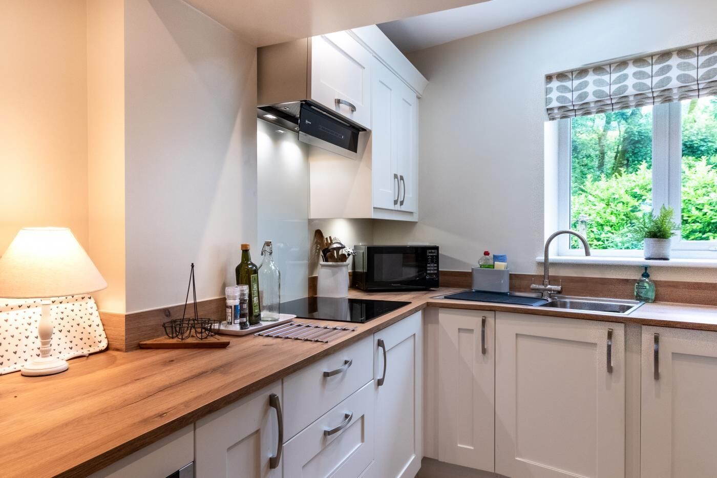 Une cuisine moderne avec des armoires blanches, un plan de travail en bois, un four à micro-ondes encastré et une fenêtre donnant sur un paysage verdoyant.