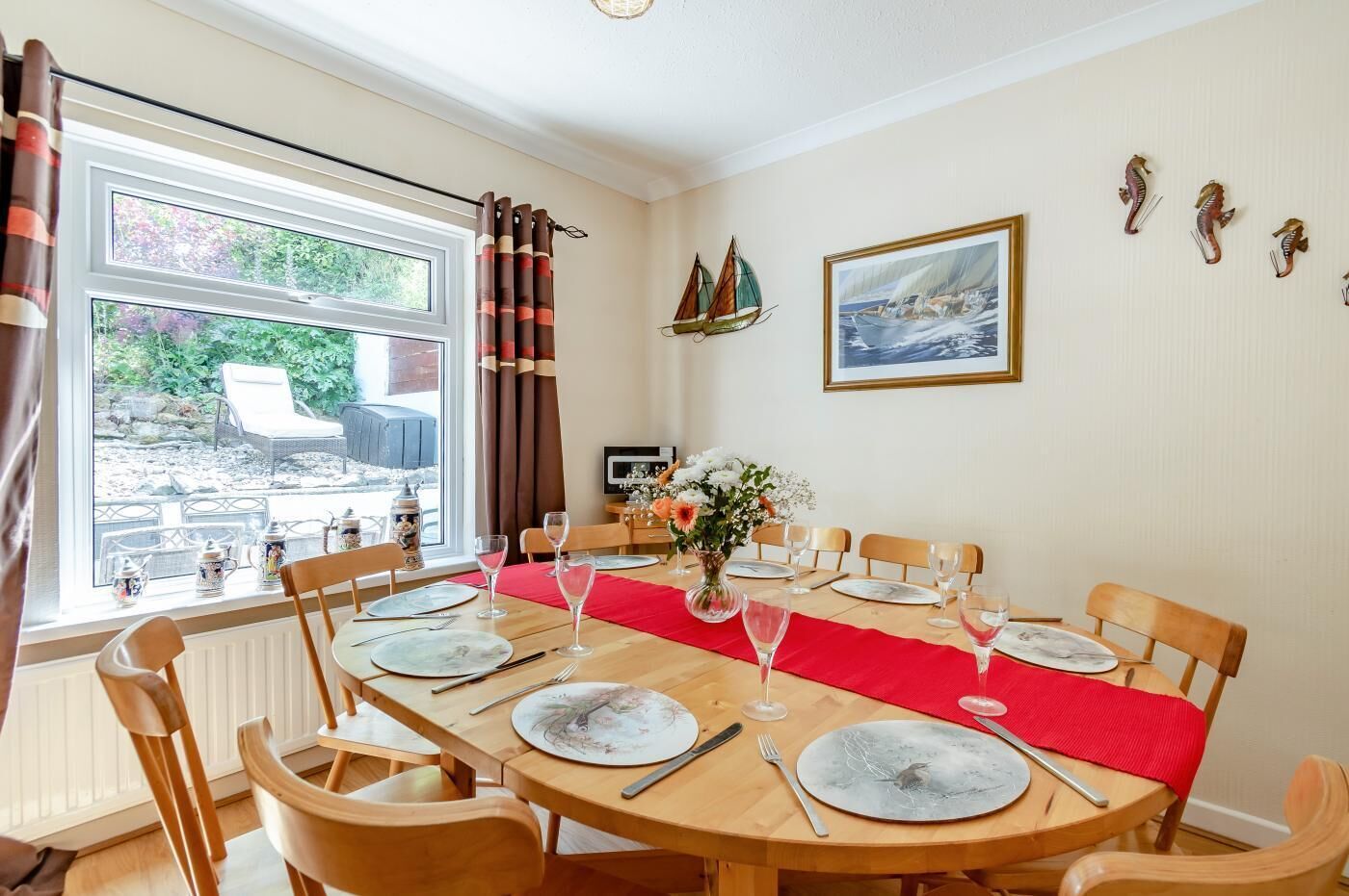 A dining area with a wooden table set for six, a red runner, and a view of the garden through the window.