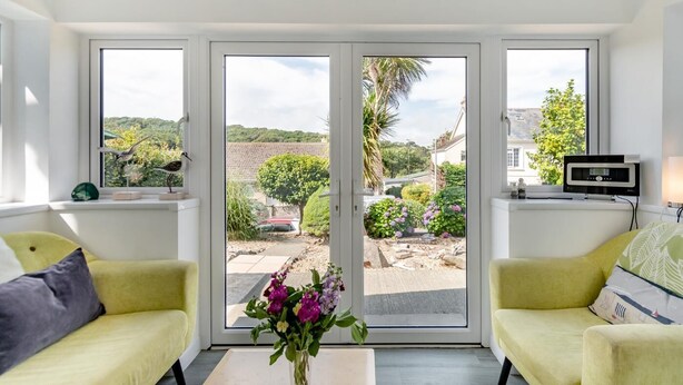 Un salon moderne avec deux canapés jaunes, une table basse et un téléviseur posé sur une étagère. De grandes fenêtres offrent une vue sur un jardin et un immeuble.