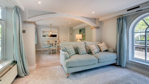 A living room with a light blue sofa, a dining area, and a large window with curtains. - 1 Bed in Whitby (oc-wa031) (Grosmont)