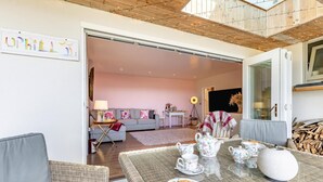 Ein gemütliches Wohnzimmer mit Essbereich, mit Korbmöbeln, einem für Tee gedeckten Tisch und einer Couch mit floralen Kissen.