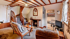 Uma sala de estar aconchegante com lareira, vigas de madeira, escada e televisão.