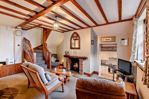 Ein gemütliches Wohnzimmer mit Kamin, Holzbalken, einer Treppe und einem Fernseher.