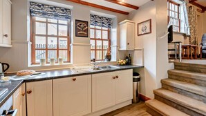 Uma cozinha com armários brancos, bancada de granito, janela com valance estampado e um certificado emoldurado na parede.