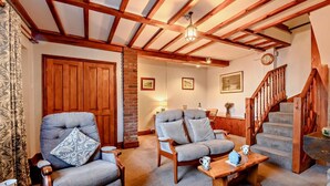Uma sala de estar aconchegante com duas poltronas, uma mesa de centro de madeira, uma escada e uma lareira de tijolos.