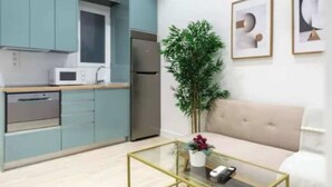 A modern kitchen with teal cabinets, a stainless steel refrigerator, and a microwave. There is a glass coffee table with a vase of flowers. - AR Movistar Arena/Wizink centrally located and modern floor (Madrid)